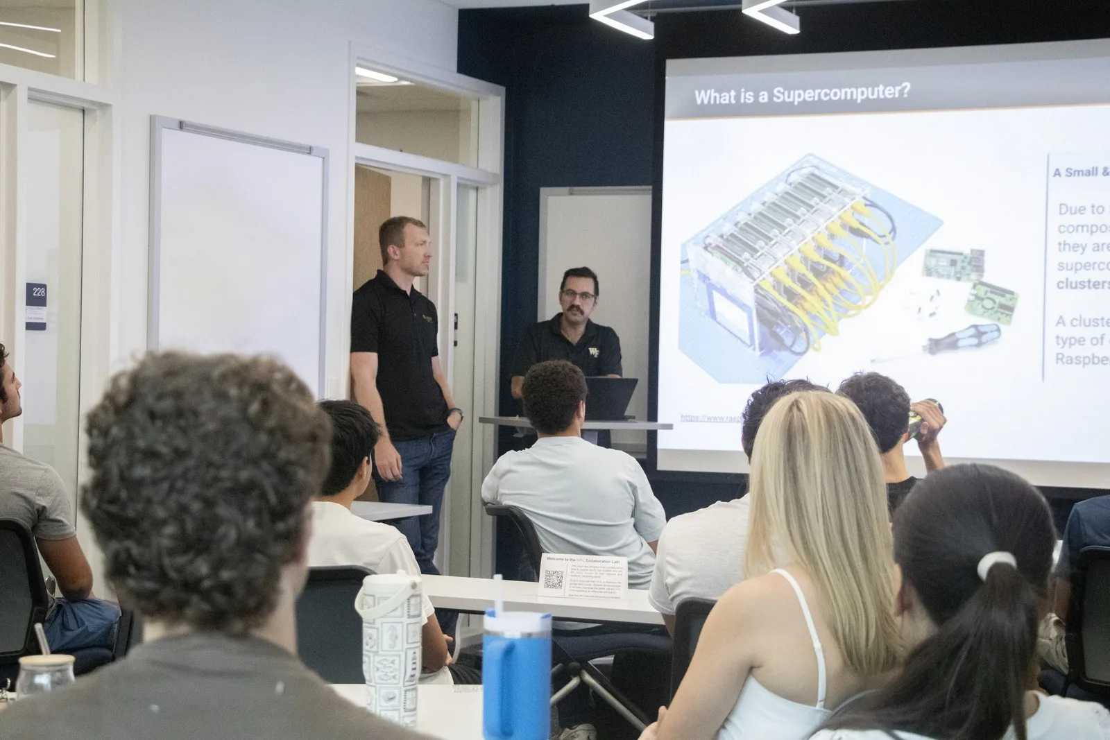 Students face two presenters and a projected slide titled “What is a Supercomputer?”